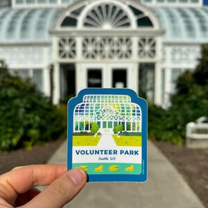 May include: A blue and green sticker with a white illustration of a greenhouse and the text "VOLUNTEER PARK Seattle, WA".
