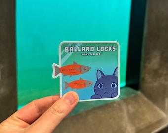 May include: A blue and green sticker with the text "Ballard Locks Seattle WA". The sticker features two orange fish and a blue cat with big eyes.