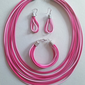 May include: A pink and white layered necklace, bracelet, and earrings set. The jewelry is made of multiple strands of thin, pink and white cord.
