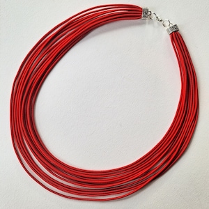 May include: A red multi-strand necklace with silver clasps. The necklace is made of thin, flexible cords.