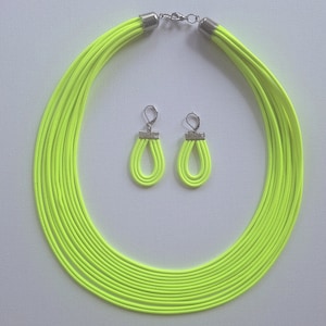Peut inclure: Un collier multi-brins jaune néon et des boucles d'oreilles assorties. Le collier est composé de plusieurs brins de cordon fin jaune vif. Les boucles d'oreilles sont simples et pendantes, également en cordon jaune.