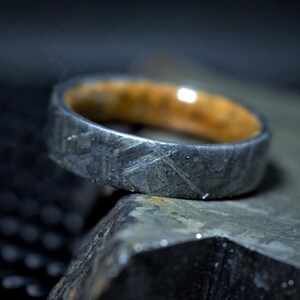 May include: A close-up of a ring with a dark, textured exterior and a light brown interior. The ring is resting on a dark, textured surface. The ring's exterior has a unique, patterned design.
