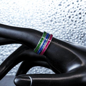 May include: Three thin metal rings stacked together, each featuring a vibrant inlay. The first ring has a bright green glitter inlay, the second a deep blue glitter inlay, and the third a vivid magenta pink glitter inlay, all set in a polished silver-tone band.