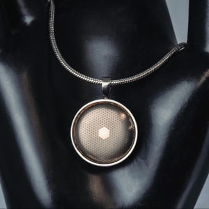 May include: Silver-toned necklace featuring a round pendant with a honeycomb pattern. The pendant has a silver frame and a light-colored center. The chain is a snake chain style. The necklace is displayed on a black mannequin.