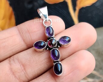 May include: Silver cross pendant with amethyst and garnet gemstones. The cross is decorated with a floral design. The pendant is approximately 2 inches in length.