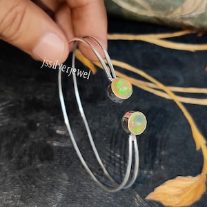 May include: A silver bangle bracelet with two opal gemstones. The bracelet is open and has a simple design.