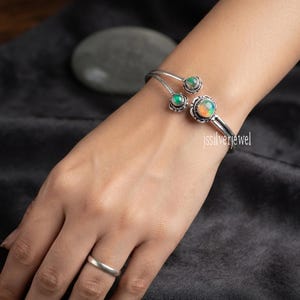 Peut inclure: Un bracelet manchette en argent orné de trois pierres cabochons rondes et irisées de tailles différentes, serties dans des montures en métal décoratives. Le bracelet présente un design ouvert et porte le texte jssilverjewel sur le métal.