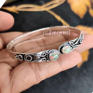 Puede incluir: Pulsera de plata con dos piedras de ópalo ovaladas. La pulsera tiene un diseño delicado y adornado con un patrón de cuerda.