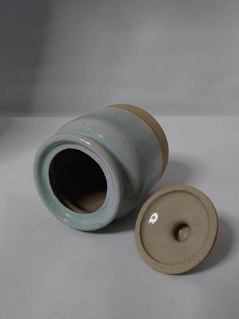 Puede incluir: Un tarro de cer&aacute;mica azul claro con tapa. El tarro tiene un borde marr&oacute;n y un esmalte moteado. La tapa tambi&eacute;n es de cer&aacute;mica y tiene un esmalte marr&oacute;n claro.