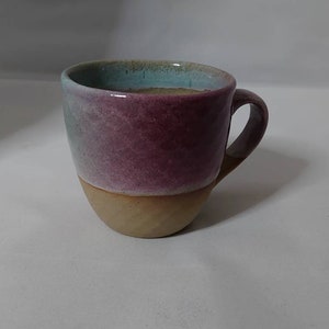 May include: A ceramic mug with a light blue, pink, and brown glaze. The mug has a rounded shape and a handle.