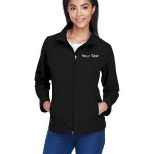 Könnte beinhalten: Schwarze Jacke mit Reißverschluss und dem Text "Your Text" auf der Brust. Die Jacke hat einen Stehkragen, zwei Vordertaschen und wird über einem weißen Shirt und blauen Jeans getragen.