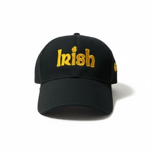 May include: Black baseball cap with the word "Irish" embroidered in gold thread across the front. A small gold shamrock is on the side. The cap has a curved brim and a structured fit.