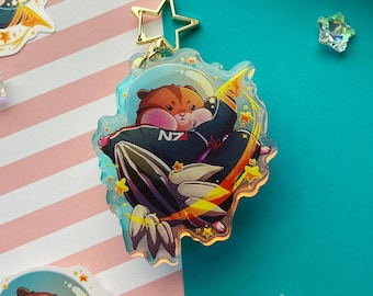 May include: A clear acrylic charm featuring a cartoon hamster in a navy blue and black space suit with the letters "N7". The hamster is riding a rocket with yellow flames and stars. The charm has a gold star-shaped clasp.