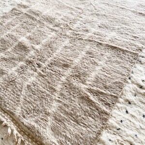 Pu&ograve; includere: Un tappeto color crema con una texture soffice e frange. Il tappeto &egrave; fatto di lana e ha un aspetto naturale e rustico.