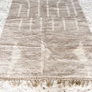 May include: A beige and white Moroccan rug with a geometric pattern. The rug has a fringe border.