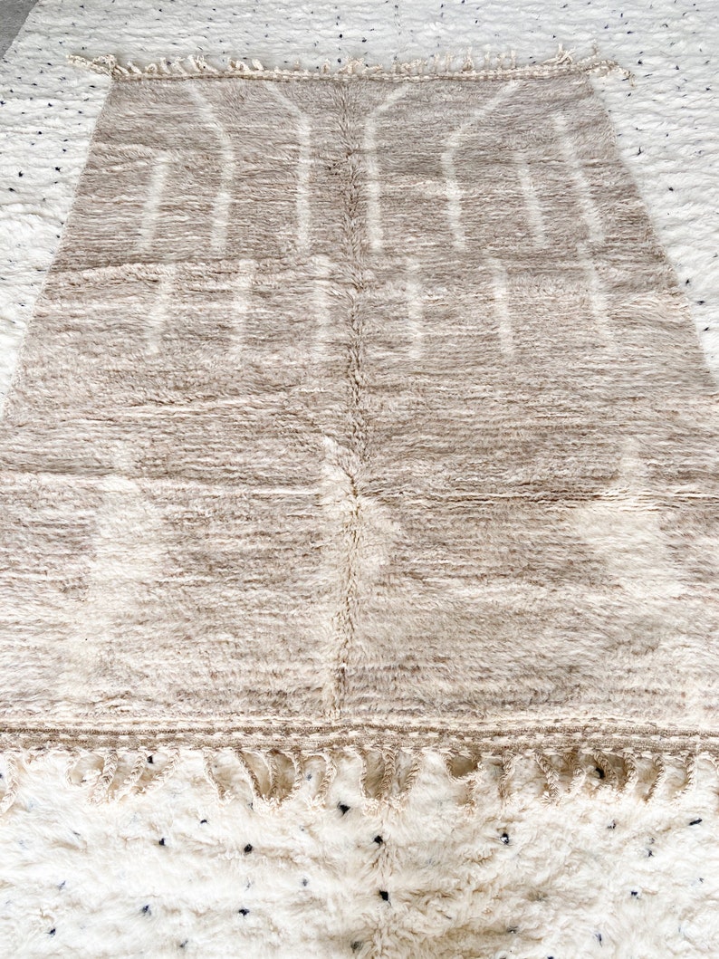 May include: A beige and white Moroccan rug with a geometric pattern. The rug has a fringe border.