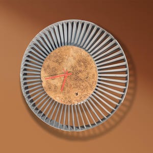 以下が含まれることがあります： ユニークなデザインの丸い壁掛け時計。時計は、木製の瘤の中心を取り囲む、薄い灰色の扇形の外側のリングが特徴です。赤い時計の針が時間を表示します。時計の直径は約30cmです。