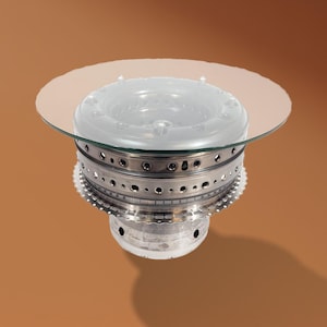 May include: A glass-topped coffee table made from a repurposed aircraft engine part. The table has a circular glass top and a metal base with a series of concentric rings.