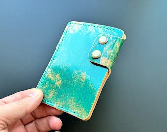 May include: A green leather card holder with a distressed finish and two silver metal snaps.