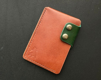 May include: A brown leather wallet with a green leather flap and two silver snaps. The wallet has a small embossed logo on the front.