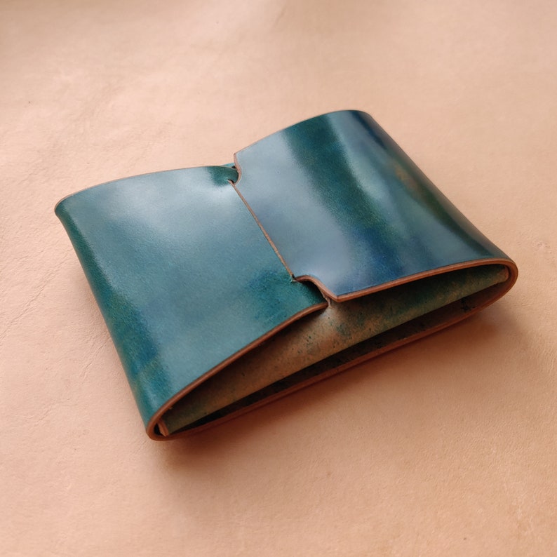 Op de afbeelding: Een teal leren portemonnee gevouwen en dicht. De portemonnee is gemaakt van glad, gepolijst leer met een subtiele glans.