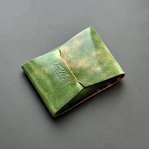 May include: Green leather wallet with a distressed finish. The wallet has a folded design with a flap closure. The embossed text "Toro Negro" is visible on the front. The wallet is made of a durable material and is likely handmade.