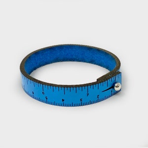 May include: A blue leather ruler bracelet with a silver metal slider. The ruler is marked with numbers from 1 to 9.