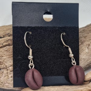 Op de afbeelding: Een paar zilveren oorhangers met bruine koffieboonbedels.