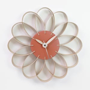 Peut inclure: Une horloge murale moderne au design unique. Le cadran de l'horloge est un disque circulaire de couleur corail avec des aiguilles argentées. L'horloge est entourée d'un anneau de 12 pétales en bois, créant une forme de fleur.