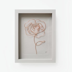 Könnte beinhalten: Eine gerahmte Skulptur aus Kupferdraht in Form einer Rose, mit einem weißen Passepartout und einem weißen Rahmen.