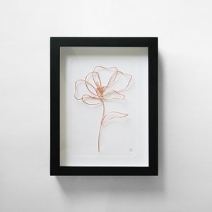 Könnte beinhalten: Eine gerahmte Skulptur aus Kupferdraht einer Blume mit einem einzigen Stiel und Blatt. Die Skulptur befindet sich auf einem weißen Hintergrund.
