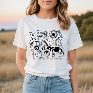 May include: White t-shirt with a black and white graphic design of farm animals, vegetables, and a tractor. The text "Support Your Local Farmers" is printed below the graphic.