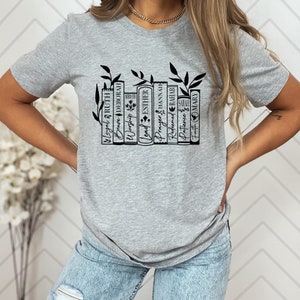 May include: Gray t-shirt with a black graphic of a bookshelf with books titled "Worship", "Lead", "Prayer", "Redeemed", "Patience", "Truth" and names like "Deborah", "Ruth", "Esther", "Hannah", "Sarah", and "Mary".