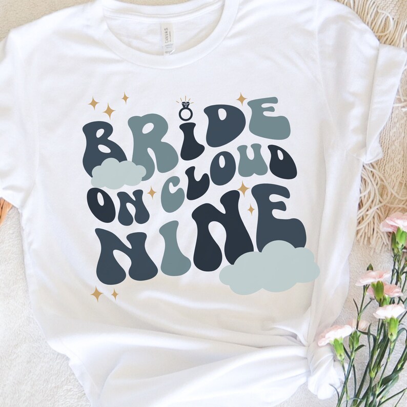 May include: White t-shirt with a blue and gray graphic that says "Bride on Cloud Nine" with a gold ring and stars.