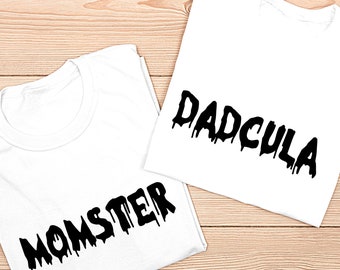 May include: Two white t-shirts with black dripping text. One shirt says "MOMSTER" and the other says "DADCULA".