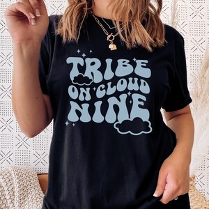 May include: Black t-shirt with a blue graphic that says "Tribe on Cloud Nine" in a retro font. The graphic includes clouds and stars.