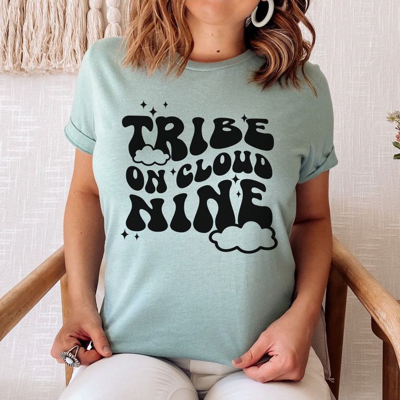 May include: A light blue t-shirt with a black graphic that says "Tribe on Cloud Nine" in a retro font. The graphic includes clouds and stars.
