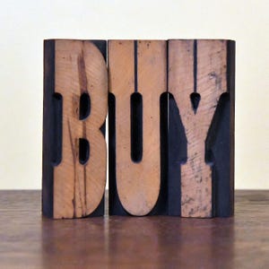 May include: Wooden letter blocks spelling the word "BUY" in black and brown. The blocks are arranged in a row.