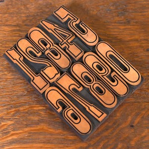 May include: A set of vintage wood printing blocks with the numbers 1234, 5671, and 0020 printed in orange on a black background.