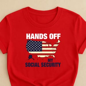 May include: Red t-shirt featuring the text "HANDS OFF" above a graphic of the United States flag and map. Below the graphic, the text reads "MY SOCIAL SECURITY" in navy blue.