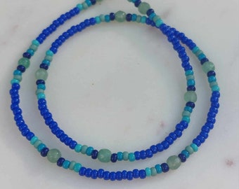 Puede incluir: Un collar de cuentas de doble cadena con cuentas azules y verdes. El collar tiene un cierre dorado.
