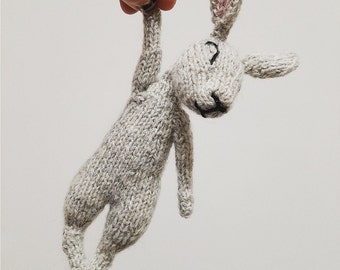May include: A gray knitted bunny rabbit toy with pink ears. The bunny is hanging from a hand.
