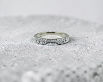 May include: A silver-toned metal ring featuring two parallel rows of small, clear, sparkling stones embedded along the entire outer circumference of the band. The ring has a polished finish and a consistent width throughout its circular design.