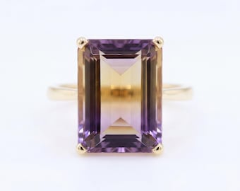 May include: A ring featuring a large, rectangular, emerald-cut ametrine gemstone with a distinct color gradient transitioning from deep purple at the top and bottom edges to a warm, golden yellow in the center, set in a simple gold band.