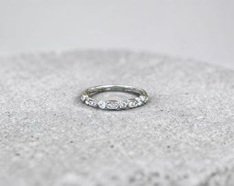 May include: A silver-toned band ring featuring an alternating pattern of round and rectangular settings, each containing a small clear stone. The metal has a polished finish, and the design creates a continuous, repeating sequence around the band.