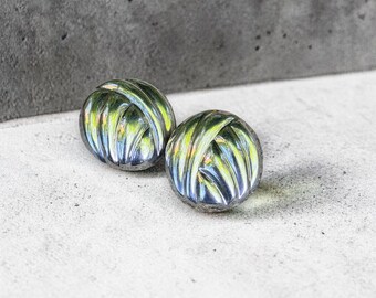 May include: A pair of round, metallic buttons featuring a swirling, ribbed pattern with a polished finish. The surface displays reflective highlights in shades of silver, dark gray, and subtle hints of yellow, creating a dimensional, textured appearance.