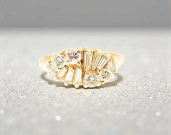 May include: A gold ring featuring a cluster of round brilliant cut diamonds and tapered baguette cut diamonds arranged in a fan-like pattern across the top of the band. The setting is crafted from polished yellow gold, highlighting the stones.