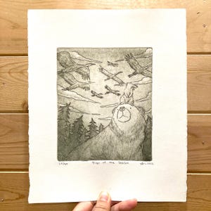 May include: A monochrome etching print titled "Sign of the Season" depicting a bear with a rabbit on its head, birds in flight, and trees. The print is on textured paper and includes the edition number 23/40. The artist's signature is visible.