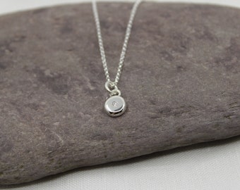 May include: A silver chain necklace with a small round pendant featuring a single diamond in the center.