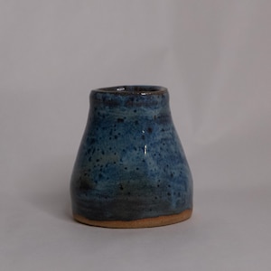 May include: A small, blue ceramic vase with a speckled glaze. The vase has a wide base and a narrow neck.